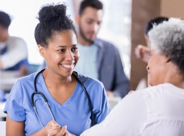 Smiling mid adult African American nurse talks with a senior woman.